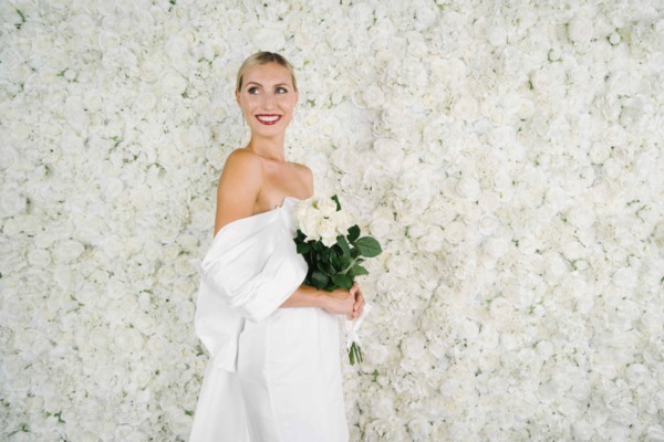 Klassische Braut vor weißer Blumenwand, Pearl White